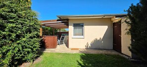Einbungalow mit überdachter Terrasse, einem eingezäunten Garten und einem kleinen Gartenbereich.