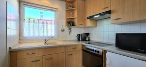A kitchen with wooden cabinets, a stainless steel sink, a stove, and a microwave.