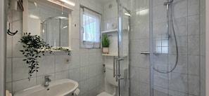 A bathroom with a glass shower enclosure, a sink, and a mirror.