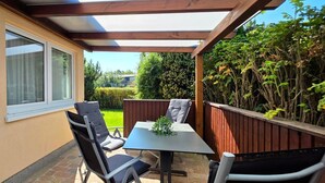 Eine Terrasse mit Tisch und Stühlen, ein Holzzaun und Blick auf einen Garten.
