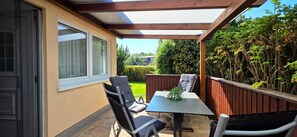 A patio with a table and chairs, a wooden fence, and a view of a garden.