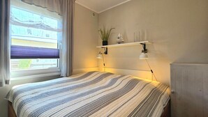 Ein Schlafzimmer mit einem Bett, einem Fenster mit Vorhängen, einem Regal mit Dekoration und einer Heizung.