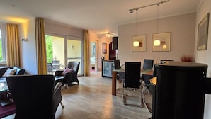 En moderne stue med sofa, stole, et spisebord og et køkken i baggrunden.