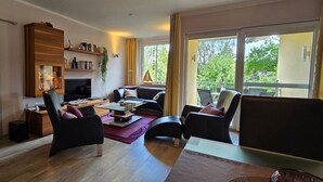 En moderne stue med sofa, stole, sofabord og fjernsyn. Der er et bogreol og en plante.