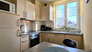 A compact kitchen with a stove, oven, microwave, and a window with curtains. - Vacation apartment L41 "Morgensonne" - 3-room apartment (approx. 54 m²) for 4 people with balcony (Graal-Müritz)