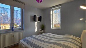 A bedroom with a bed, a TV mounted on the wall, and windows with curtains. - Vacation apartment L41 "Morgensonne" - 3-room apartment (approx. 54 m²) for 4 people with balcony (Graal-Müritz)