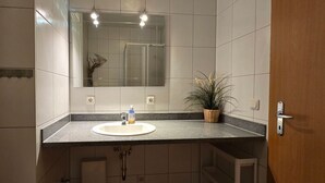 Un baño con un lavamanos blanco, un espejo y una planta en maceta.