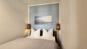 Una habitación de hotel con una cama, dos almohadas blancas, un cabecero y un cuadro colgado en la pared.