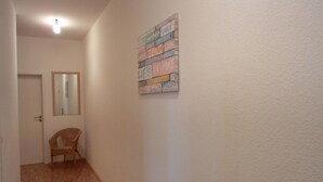 A hallway with a wooden floor, a door, a chair, and a wall-mounted artwork with various words.