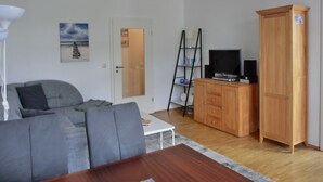 A living room with a grey sofa, a wooden cabinet with a television, and a white door.