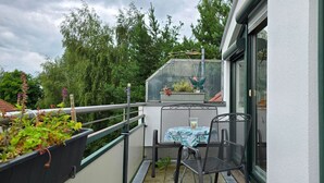 Un balcon avec une table et des chaises, un petit jardin et une serre.