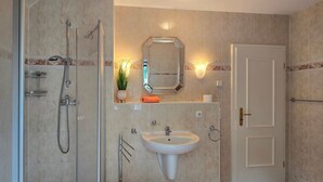 Une salle de bain avec une douche à parois de verre, un lavabo sur colonne et un miroir au-dessus du lavabo.
