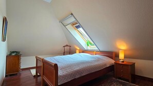 Une chambre avec un plafond en pente, un lit, des lampes de chevet, une commode et une petite fenêtre.