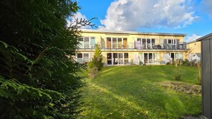 Ein zweigeschossiges Gebäude mit einem Balkon im oberen Stockwerk, einem Rasen und einem Gartenhaus.