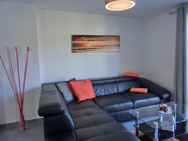 A modern living room with a black leather sofa, a glass coffee table, and a painting on the wall.