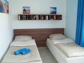 A hotel room with two beds, a wooden headboard, a bookshelf with books, and a painting above the beds.
