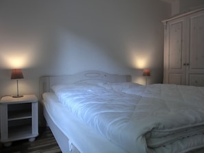 A neatly made bed with white bedding, two bedside lamps, and a white wardrobe in a simple room.