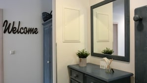 Una habitación con una puerta azul, un cartel de 'Welcome', un espejo, un aparador y una planta pequeña.