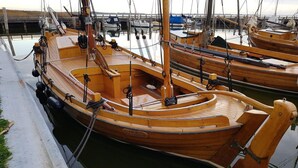 Un bateau en bois était amarré dans une marina, à côté d’autres bateaux, d’une passerelle en bois et d’une zone herbeuse.