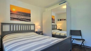 Une chambre à coucher comprenant un lit, deux tables de chevet, une chaise, un miroir et des œuvres d’art accrochées au mur.