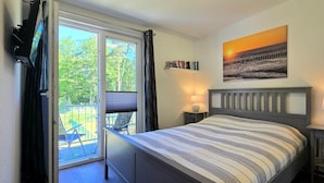 Une chambre à coucher avec un lit, une table de chevet, une lampe, un tableau et une vue sur l’extérieur.