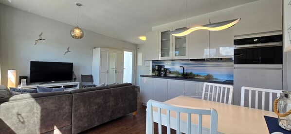 A modern living room with a sofa, TV, and dining area with a table and chairs.