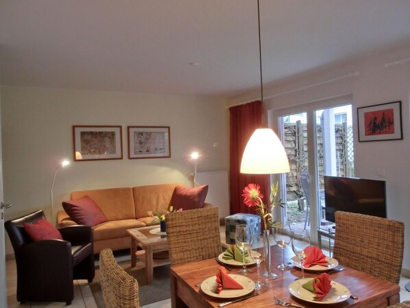 A living room with a sofa, chairs, a dining table set for two, and a TV.