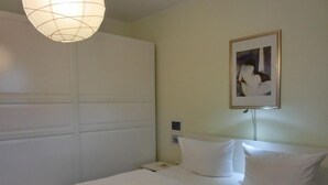 A hotel room with a bed, a bedside table, a lamp, and a framed picture on the wall. - Apartment T14 - "Blinkfüer" - 2-room apartment on the ground floor for 2 pers. (Graal-Müritz)