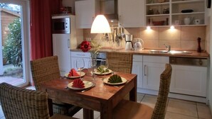 A cozy kitchen with a dining table set for four, a hanging light fixture, and a view of the outdoors. - Apartment T14 - "Blinkfüer" - 2-room apartment on the ground floor for 2 pers. (Graal-Müritz)
