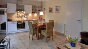 A compact kitchen with white cabinets, a dining table set for two, and a pendant light above. - Apartment T14 - "Blinkfüer" - 2-room apartment on the ground floor for 2 pers. (Graal-Müritz)