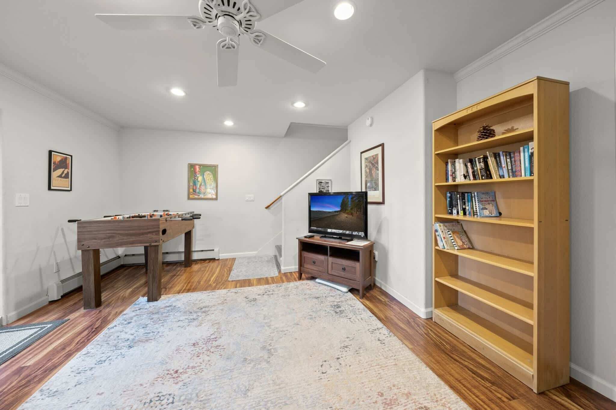 Ein Wohnzimmer mit Tischfußball, Flachbildfernseher, Bücherregal und Deckenventilator.