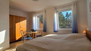 A bedroom with a bed, a wooden wardrobe, a table with chairs, and a window with curtains.