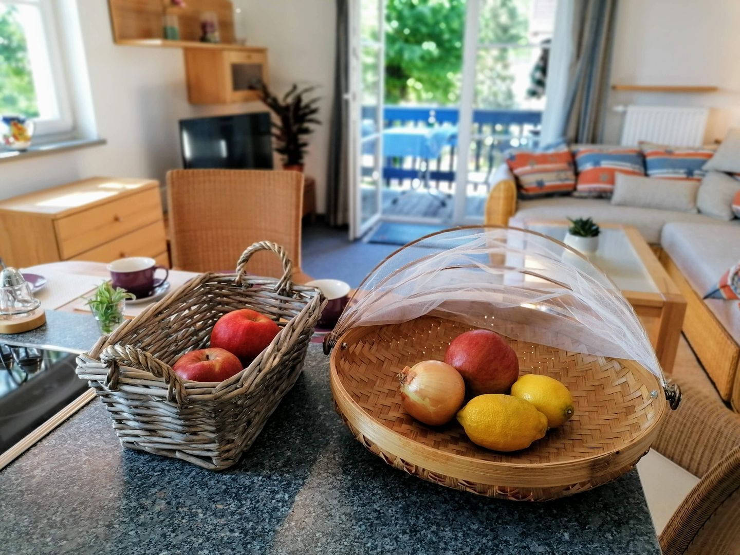 A kitchen area with a wicker basket containing apples and a glass bowl with lemons and an onion.