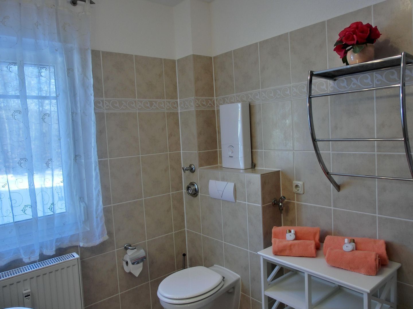 A bathroom with a toilet, a towel rack with towels, a radiator, and a shower area.