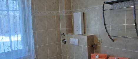 A bathroom with a toilet, a towel rack with towels, a radiator, and a shower area.