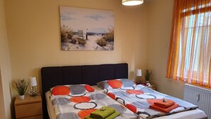 A bedroom with a bed, a nightstand, a lamp, a window with curtains, and a painting on the wall.