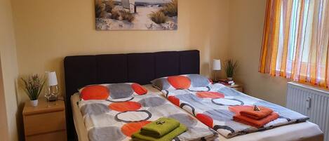 Un dormitorio con cama, mesita de noche, lámpara, ventana con cortinas y un cuadro en la pared.