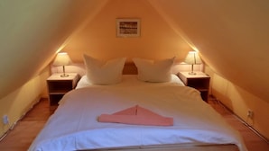 Una camera da letto mansardata accogliente, a forma di triangolo, con un letto, due lampade da comodino e un quadro appeso al muro.