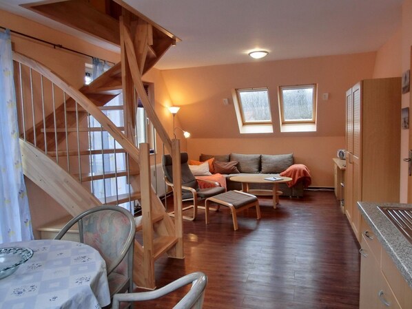 Un salon chaleureux avec un escalier en bois, un ensemble de canapés, une table à manger et un coin cuisine.