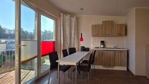 A modern kitchen with wooden cabinets, a dining table with chairs, a coffee maker, and a potted plant.