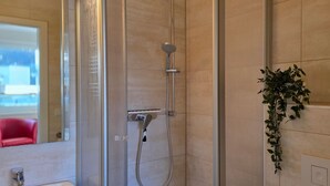A bathroom with a shower, a mirror, and a potted plant.