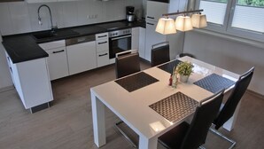 A modern kitchen with white cabinets, a black countertop, and a dining area with a white table and black chairs. - Apartment KWF 2b OG - 3-room apartment with 2 bedrooms for 6 people with WLAN (Gelbensande)
