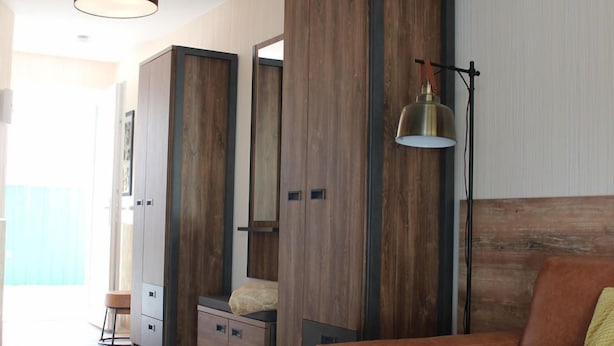 Ein modernes Hotelzimmer mit einem Holzschrank, einer Ledersofa, einem kleinen runden Tisch und einer Stehlampe.