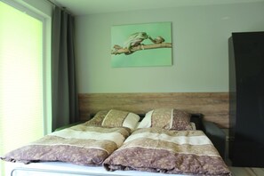 A bed with a patterned bedspread, a wooden headboard, and a green wall with a framed picture of a frog.
