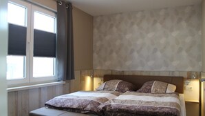A bedroom with a bed, two bedside lamps, a window with curtains, and a patterned wall.