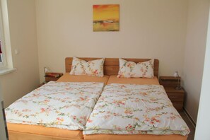 A double bed with floral bedding, two bedside tables, a nightstand, a lamp, and a painting on the wall.