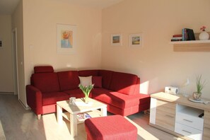 En rød sofa, et lille bord med en blomstervase, og et skrivebord med en radio samt dekorative genstande.