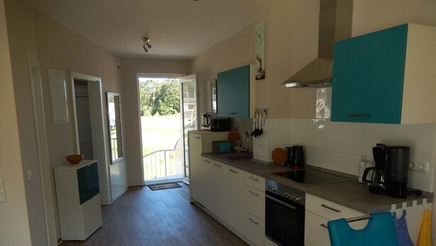 A modern kitchen with white and teal cabinets, a microwave, coffee maker, and a view to the outside.