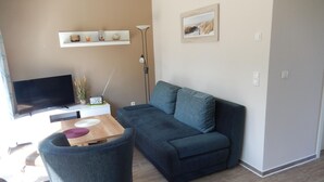 A modern living room with a dark grey sofa, a flat-screen TV, a wooden coffee table, and a small side table with a radio.