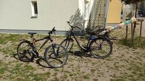 Two bicycles parked on a gravel surface in front of a building with a staircase and a window.